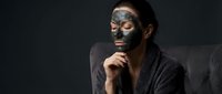 Young Asian woman applying black charcoal face mask for skincare routine, spa treatment and beauty wellness in dark moody lighting for cosmetic advertising.