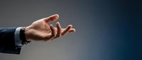 Caucasian male hand in business suit reaching out with open palm gesture against neutral gray background for corporate communication concepts.