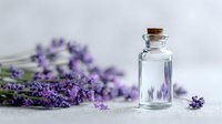 Small glass bottle with cork stopper next to fresh lavender flowers on light background, representing aromatherapy and natural cosmetics.