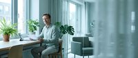 Professional businessman working at modern office desk with plants and natural light creating productive workspace atmosphere.