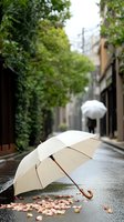 White umbrella with wooden handle on wet street with scattered pink petals, blurred silhouette with umbrella in background creates atmospheric rainy day scene.
