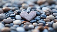Pink heart-shaped stone stands out among smooth gray and brown river pebbles, creating romantic zen composition for wellness, meditation and mindfulness practices.
