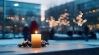 Glowing candle with pine branches against blurred winter cityscape background, creating atmospheric holiday mood with bokeh lights and snow.