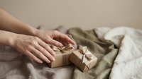 Female hands arranging small kraft paper gift boxes with twine bows on neutral linen fabric for special occasions and celebrations.