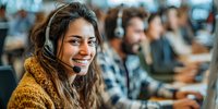 Smiling young woman with headset working in busy customer service center, wearing mustard sweater among diverse colleagues.