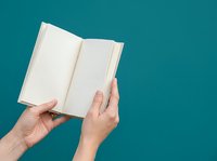 Person holding open blank notebook with empty pages against teal background for education, writing, journaling, or publishing mockup purposes.