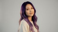 Young Asian woman with purple ombre hair smiling confidently in casual white sweater against neutral background for lifestyle and beauty content.