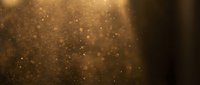 Golden bokeh particles floating in warm amber light creating magical atmospheric background for luxury designs and festive celebrations.