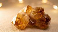 Amber crystals with warm golden tones clustered together on neutral surface with soft bokeh lighting, suitable for gemstone, mineral, and wellness content.
