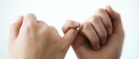 Two hands making a pinky promise gesture, symbolizing trust, commitment, and friendship between people on a light background.