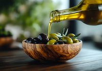 Pouring golden extra virgin olive oil over fresh mixed olives in wooden bowl, close-up shot with natural lighting and blurred background.