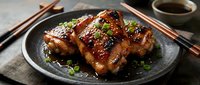 Glazed grilled pork ribs with sesame seeds and green onions served on dark plate with chopsticks and soy sauce for Asian cuisine dining experience.