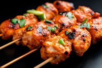 Grilled chicken skewers with spicy marinade and fresh herbs on wooden sticks against dark background, close up view showing juicy charred meat texture.