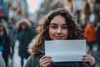 Young Latin American woman with curly hair holding blank white paper mockup in crowded urban street. Perfect for advertising, protest concepts or communication designs.