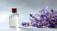 Lavender essential oil in small glass bottle with cork stopper next to dried lavender flowers on light background, for aromatherapy and natural skincare.