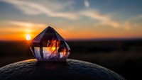 Crystal prism refracting golden sunset light on rocky surface with dramatic sky background for meditation and spiritual wellness concepts.