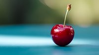 Fresh red cherry with stem on blue surface against soft blurred background for healthy eating and summer fruit concepts.