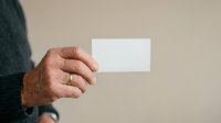 Male hand holding blank white business card against neutral beige background, suitable for branding, corporate identity, and marketing mockup projects.
