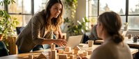 Professional businesswoman presenting strategy with wooden blocks to colleague in modern office workspace with natural lighting and plants.