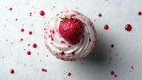 Fresh strawberry cupcake with white cream frosting and red berry splashes on light background, decorated with whole ripe berry on top. Food photography.