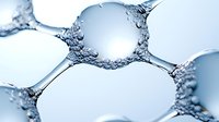 Microscopic view of soap bubbles or foam cells showing delicate membrane structures and surface tension patterns in cool blue tones, scientific macro photography.