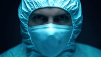 Medical professional wearing protective surgical mask and cap in dramatic blue lighting, focused intense eyes visible above mask for healthcare concepts.
