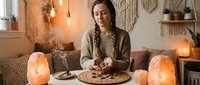 Young African American woman enjoying cozy evening with cookies and warm lighting in bohemian living room with salt lamps and macrame wall decor.