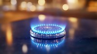 Blue gas stove flame burning on dark kitchen counter with warm bokeh lights in background, close up view showing energy consumption and cooking concept.