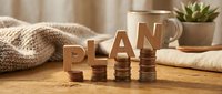 Financial planning concept with wooden PLAN letters and stacked coins on rustic table with cozy home decor elements for budgeting and investment strategies.