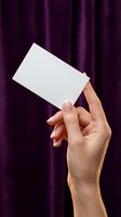 Female hand holding blank white business card against purple velvet curtain background for branding and corporate identity mockup presentations.
