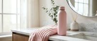 Insulated water bottle in dusty rose on bathroom vanity with towel, mirror, and plant decor for home interior design projects.