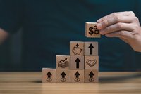 Hand placing wooden blocks with business growth icons in ascending steps formation for financial success concepts.