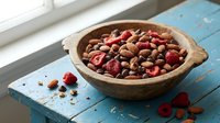 Wooden bowl filled with mixed nuts and dried cranberries on rustic blue table near window. Healthy snacking and organic food concept for kitchen decor.