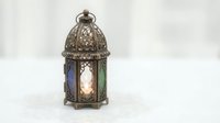 Ornate metal lantern with stained glass panels in blue and green, featuring intricate filigree detailing and dome top, casting ambient light for home decor and events.
