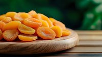 Dried apricots on wooden cutting board against dark green background, healthy organic snack food, natural dried fruit for nutritious eating.