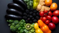 Fresh colorful fruits and vegetables arranged in rainbow pattern on dark background, including eggplant, blackberries, corn, oranges, tomatoes, peppers, broccoli and kiwi.