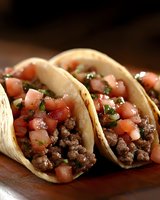 Traditional Mexican street tacos with seasoned ground beef, fresh diced tomatoes, and chopped cilantro served in warm corn tortillas on wooden surface.