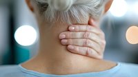 Mature woman massaging painful neck area, suffering from chronic tension and muscle strain against blurred background with bokeh lights.