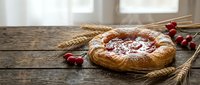 Homemade cherry pie with golden crust dusted with powdered sugar on rustic wooden table with wheat stalks and fresh red cherries for baking dessert.