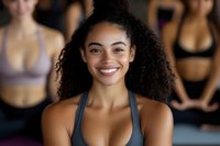 Happy young African American woman smiling in fitness class wearing sports bra with diverse group of female athletes exercising in background at gym.
