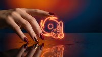 Manicured hand holding glowing neon gamepad controller symbol against dark background with orange and blue lighting, suitable for gaming, technology, and entertainment design projects.