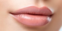 Close up of plump, naturally glossy lips wearing nude pink lipstick on light skin tone, showing perfect lip care and makeup application technique.