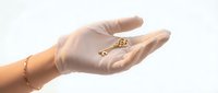 Female hand wearing gold bracelet holding ornate golden key against white background. Elegant jewelry accessory for luxury lifestyle concepts.