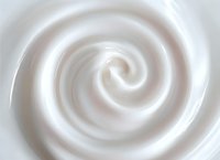 Smooth white cream swirl forming elegant spiral pattern on light background, soft creamy texture with gentle curves and shadows creates luxurious cosmetic feel.