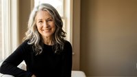 Happy mature Caucasian woman with gray hair smiling warmly in black sweater by window. Professional portrait for lifestyle and wellness content.