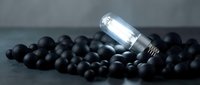 Clear glass bottle with silver cap lying on scattered black spheres against dark gray surface, suitable for product photography, cosmetics packaging mockups, and skincare branding concepts.