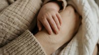Pregnant woman in cozy beige knit sweater gently touching her belly bump, expecting mother in soft neutral tones showing maternal care and love.