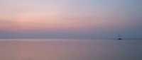 Serene seascape at dusk with calm waters reflecting soft pink and purple hues across the horizon, distant sailboat silhouette, tranquil seascape for travel and nature projects.