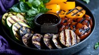 Grilled vegetables and mushrooms on black plate with balsamic sauce. Fresh colorful seasonal produce with charred grill marks served with dipping sauce.