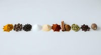 Colorful assortment of aromatic spices arranged in a row on a white background, including turmeric, pepper, paprika, cinnamon, and cardamom.
